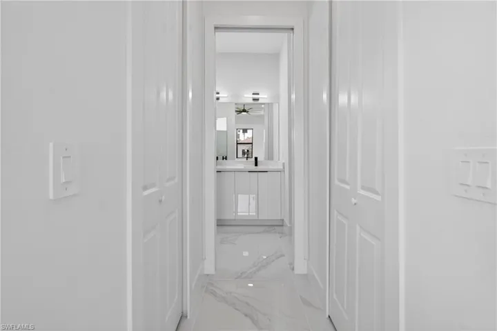 Modern hallway leading to a bathroom featuring a vanity with a white countertop, contemporary light fixtures, and a ceiling fan