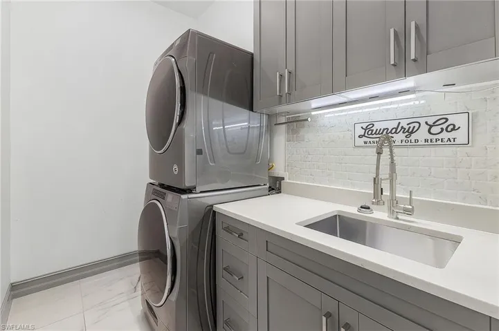 Clothes washing area featuring stacked washer / dryer, cabinets, sink, and light tile floors