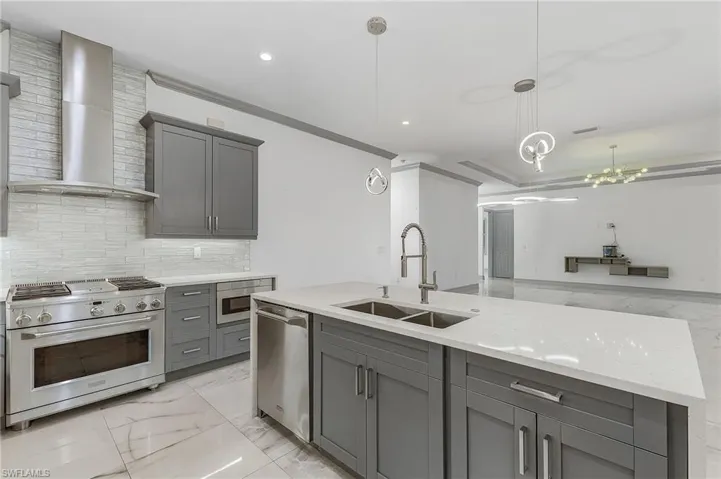 Kitchen with decorative light fixtures, light stone counters, wall chimney range hood, sink, and appliances with stainless steel finishes