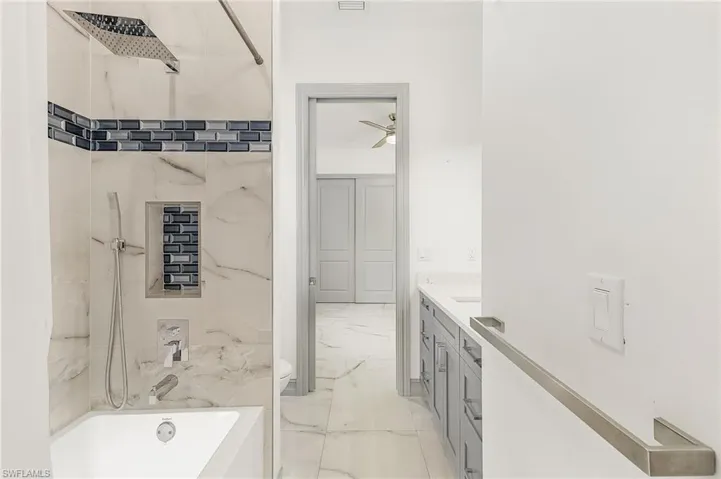 Full bathroom with ceiling fan, toilet, tiled shower / bath combo, tile flooring, and vanity