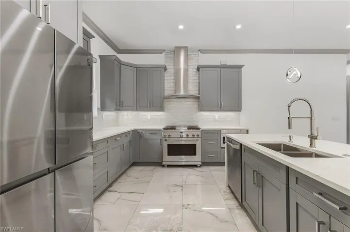 Kitchen with wall chimney range hood, stainless steel appliances, backsplash, sink, and light tile floors
