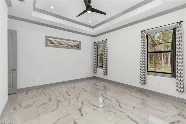 Spare room with ceiling fan, a tray ceiling, crown molding, and light tile floors