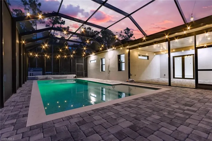 Pool at dusk featuring glass enclosure and a patio area