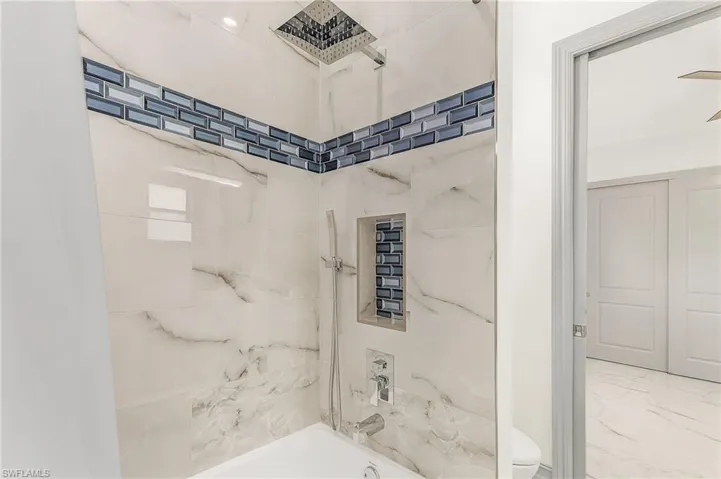 Bathroom featuring tile flooring, tiled shower / bath combo, and toilet