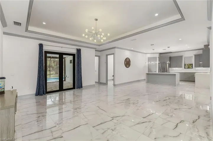 Unfurnished living room with french doors, a tray ceiling, light tile floors, and crown molding