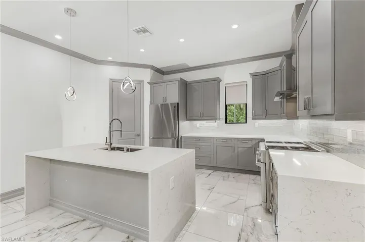 Kitchen featuring backsplash, a kitchen island with sink, appliances with stainless steel finishes, sink, and pendant lighting