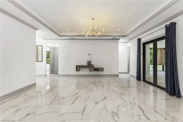 Unfurnished room featuring a tray ceiling, french doors, light tile floors, and an inviting chandelier