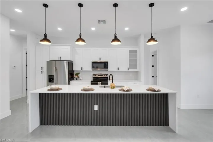 Kitchen with light stone countertops, a spacious island, glass fronted cabinets, and stainless steel appliances