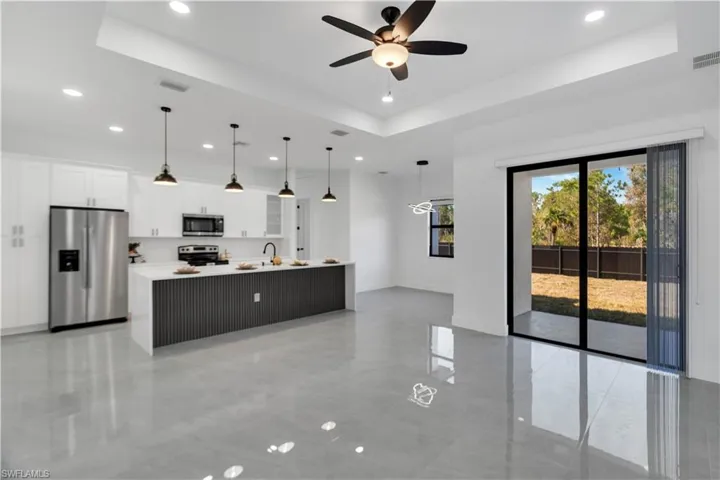 Kitchen with a tray ceiling, stainless steel appliances, a kitchen island with sink, pendant lighting, and white cabinetry