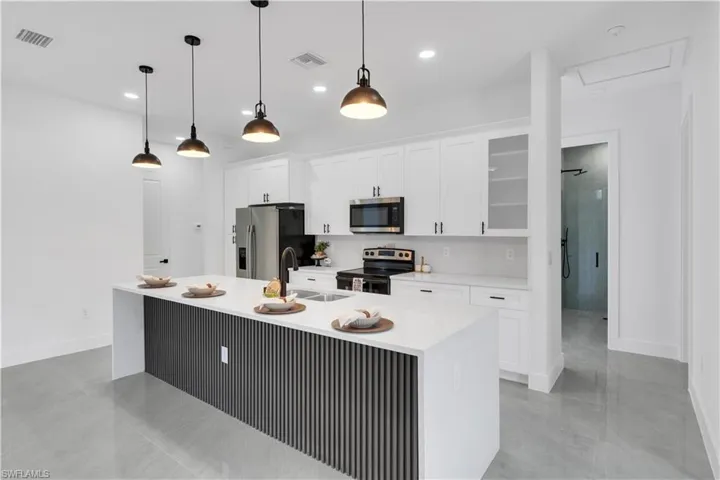 Kitchen featuring stainless steel appliances, white cabinetry, light stone counters, pendant lighting, and glass insert cabinets