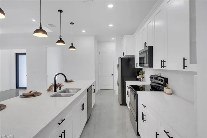 Kitchen featuring stainless steel appliances, light stone counters, white cabinetry, and decorative light fixtures