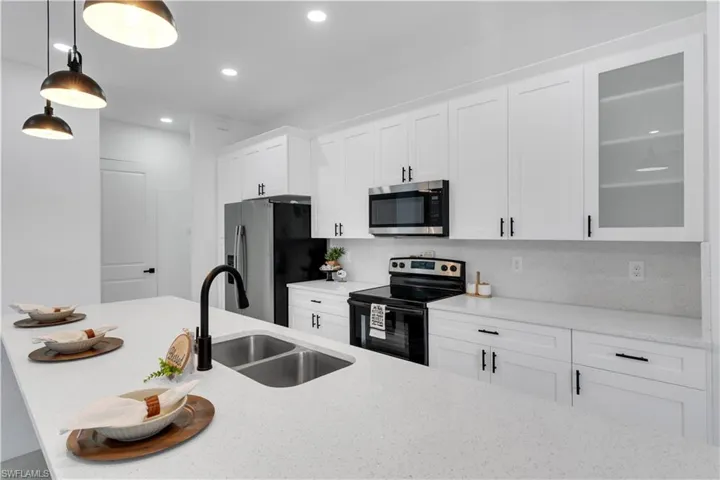 Kitchen with stainless steel appliances, white cabinetry, light stone countertops, pendant lighting, and decorative backsplash
