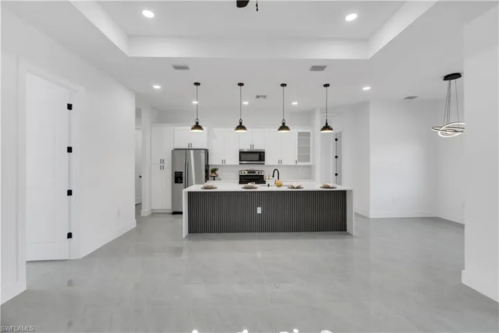 Kitchen featuring a large island, white cabinetry, glass insert cabinets, stainless steel appliances, and hanging light fixtures