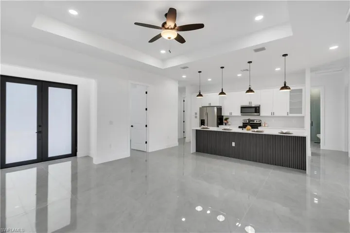 Kitchen featuring white cabinetry, a ceiling fan, stainless steel appliances, pendant lighting, and a large island with sink