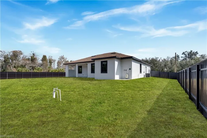 Rear view of house with a fenced backyard, stucco siding, and lawncare items