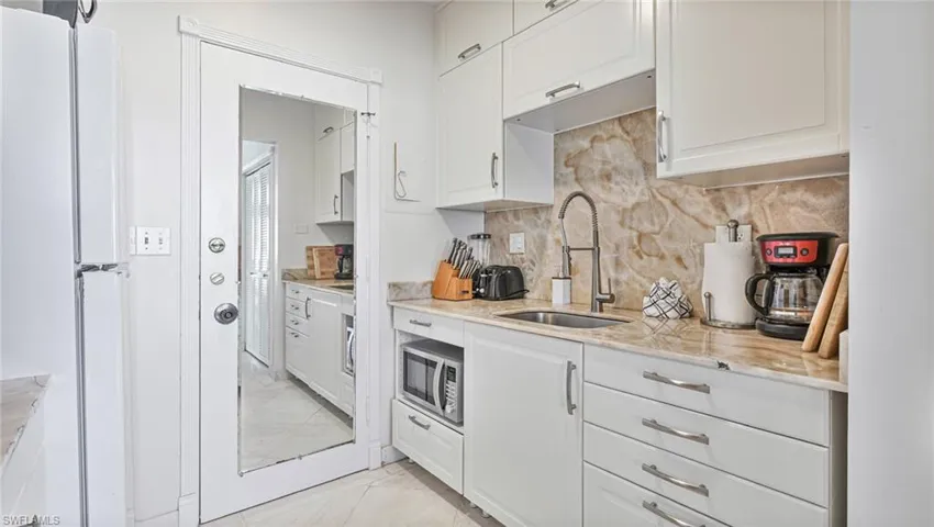 Kitchen with stainless steel microwave, decorative backsplash, sink, and white cabinetry