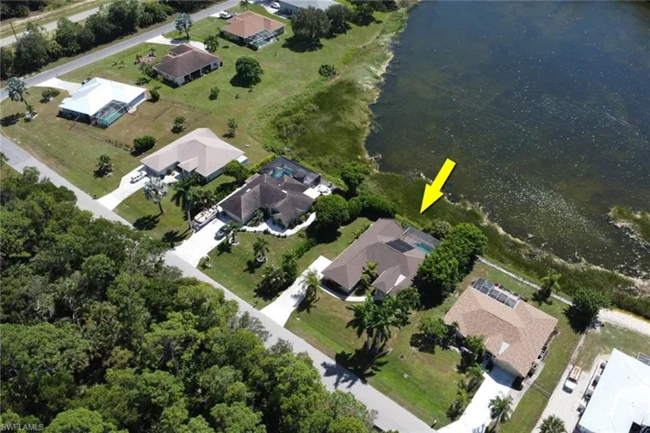 Aerial view of the property with a private pool, set alongside a body of water, and surrounded by lush greenery and other properties