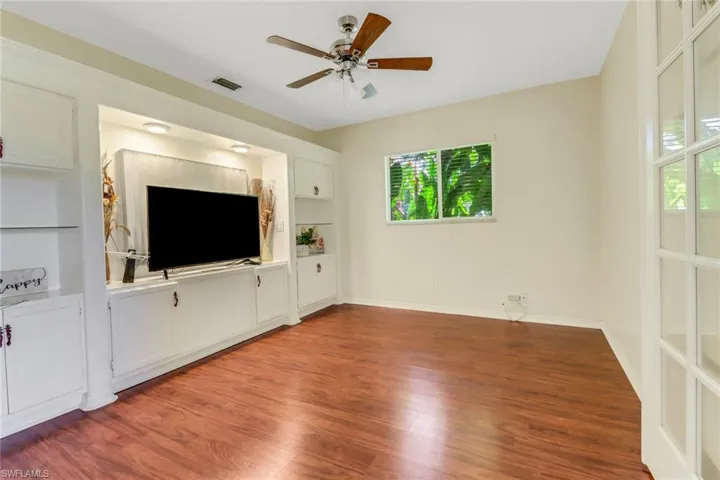 This room features wood flooring, a ceiling fan, and a window with blinds