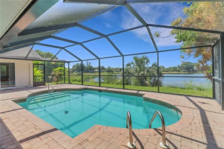 The property features a screened-in pool area with a brick paver deck, overlooking a lake and lush greenery