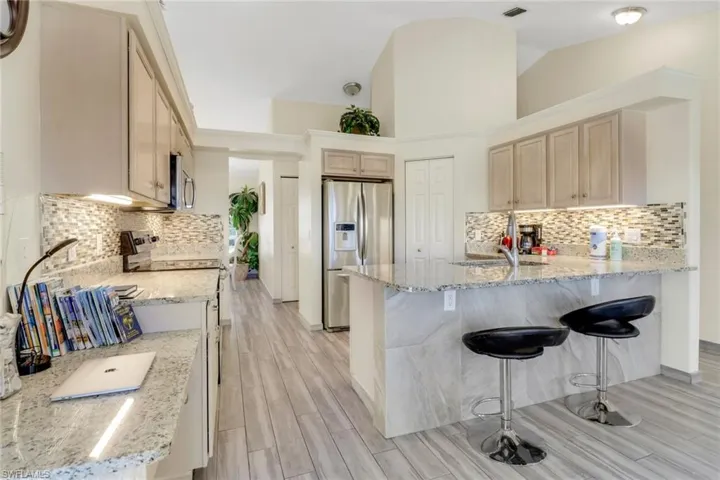 The kitchen features granite countertops, stainless steel appliances, light-toned cabinetry, and a mosaic tile backsplash