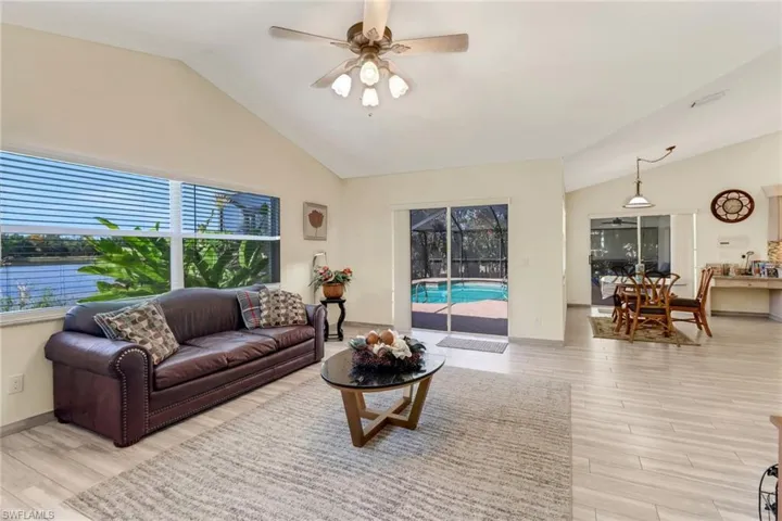 The living area features vaulted ceilings, light-toned flooring, and large windows showcasing views of the water