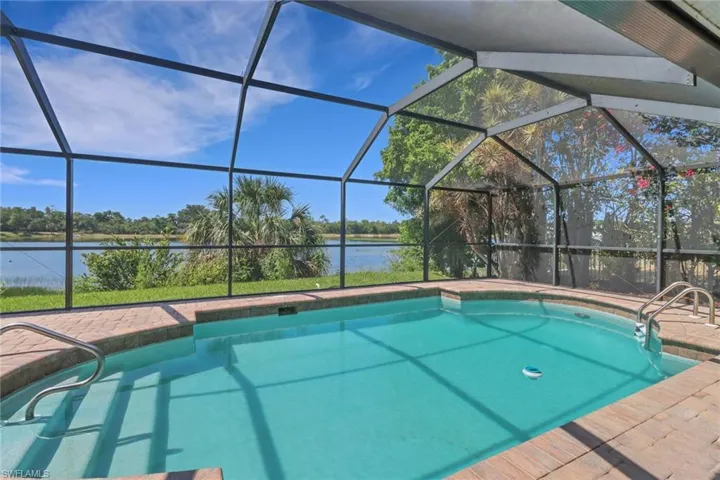 The property features a screened-in swimming pool with an integrated spa, surrounded by brick paving and overlooking a body of water with lush landscaping