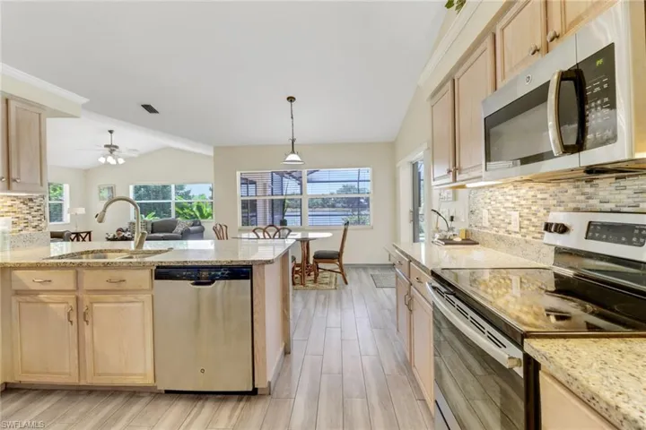 The kitchen features light-toned cabinetry, granite countertops, stainless steel appliances, and a tiled backsplash