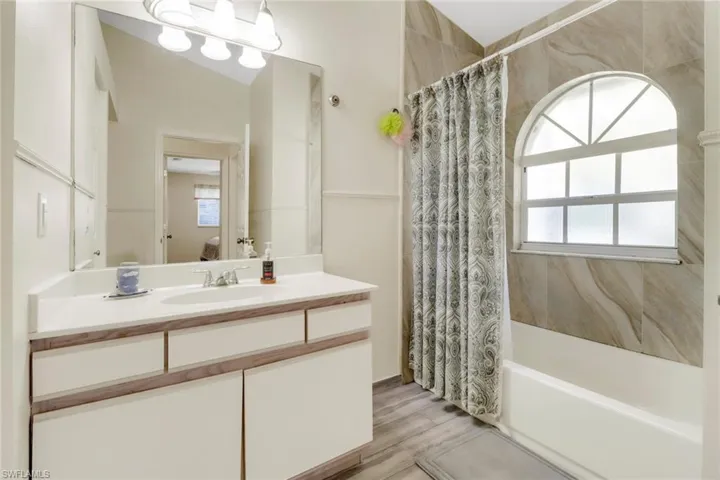 This bathroom features a vanity with a white countertop and a sink, a large mirror, and an overhead light fixture