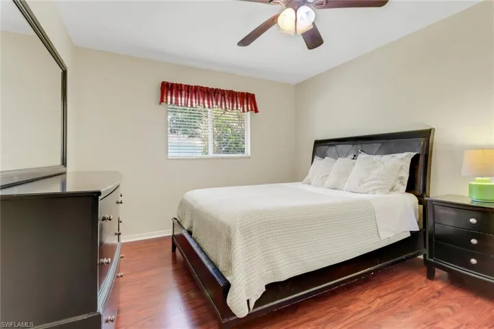This room features rich hardwood flooring, a ceiling fan, and a window with blinds providing natural light
