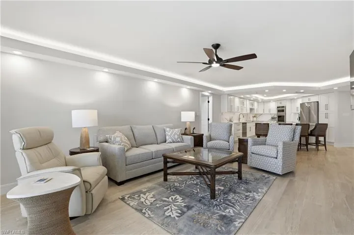 Open-concept living space featuring wood-finish flooring, recessed perimeter cove lighting, a central ceiling fan, and white cabinetry