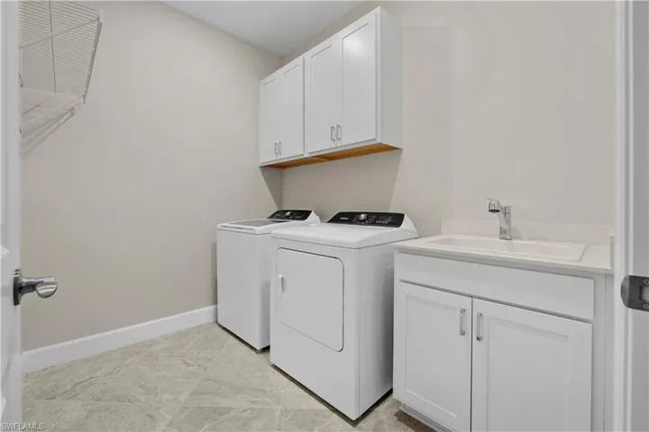 Laundry area featuring white cabinetry, a utility sink with a chrome faucet, and gray-toned tile flooring
