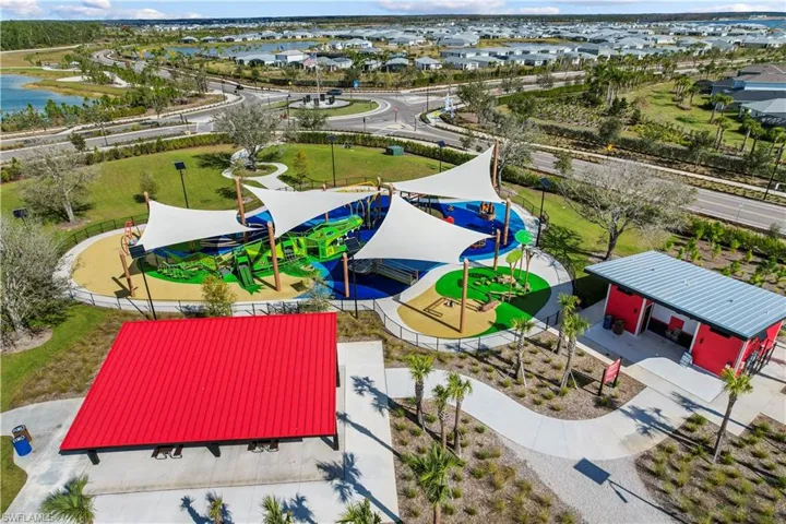 Expansive community park featuring a playground with shade canopies, a vibrant mural, a covered picnic area, and a red-sided amenity building