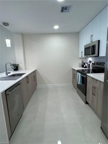 Kitchen with sink, dishwashing machine, white cabinets, stove, and pendant lighting