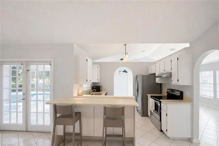 Kitchen with arched walkways, stainless steel electric stove, a kitchen breakfast bar, and light tile patterned flooring