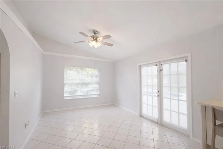 Empty room with vaulted ceiling, arched walkways, ceiling fan, light tile patterned flooring, and french doors