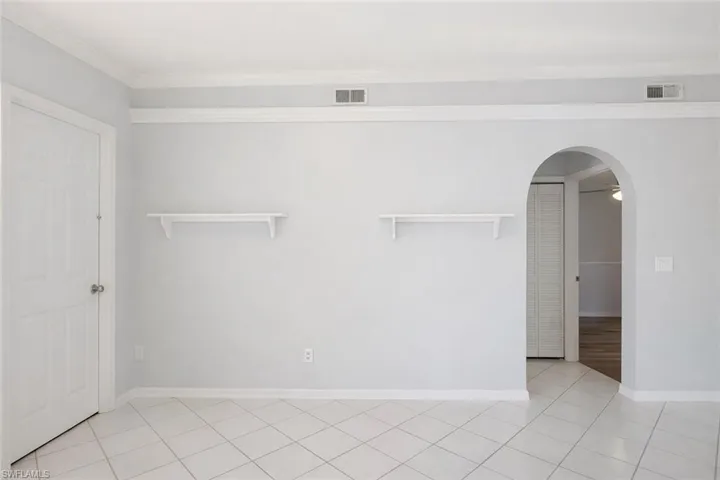 Unfurnished room with arched walkways, light tile patterned flooring, and ornamental molding