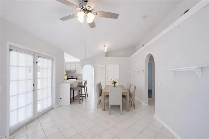 Dining space featuring lofted ceiling, a ceiling fan, light tile patterned floors, french doors, and arched walkways