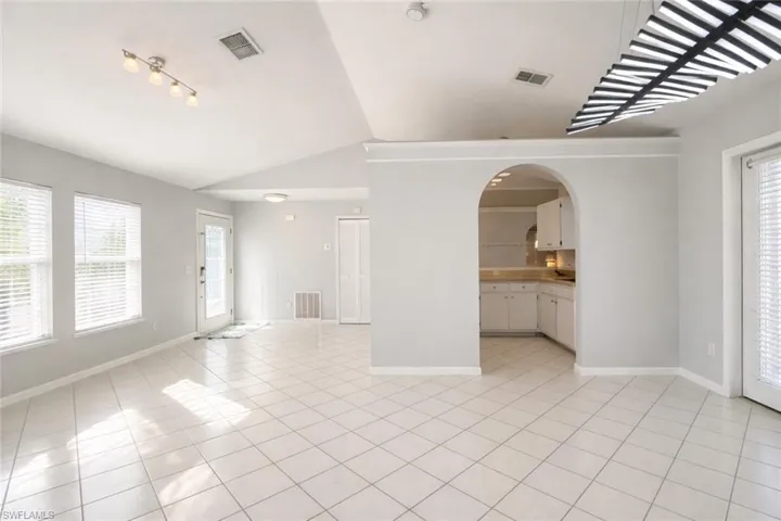 Unfurnished living room featuring healthy amount of natural light, vaulted ceiling, arched walkways, and light tile patterned floors