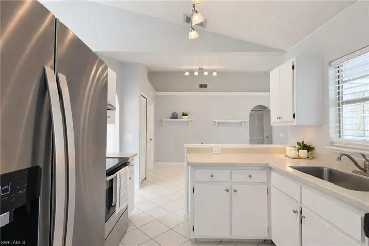 Kitchen with appliances with stainless steel finishes, a peninsula, white cabinets, vaulted ceiling, and light tile patterned flooring