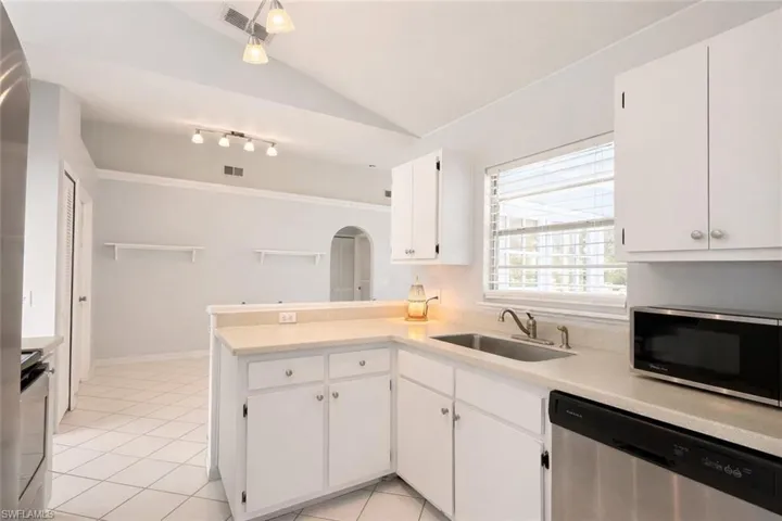 Kitchen with appliances with stainless steel finishes, a peninsula, light countertops, vaulted ceiling, and light tile patterned flooring