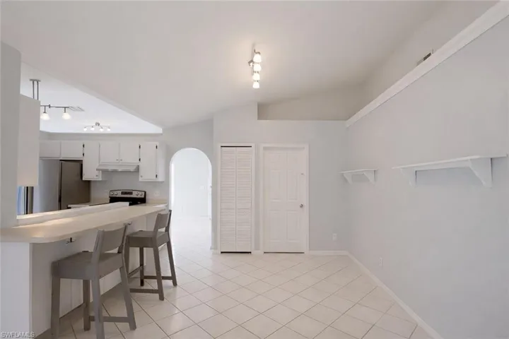 Kitchen with arched walkways, light countertops, white cabinetry, a breakfast bar, and light tile patterned flooring