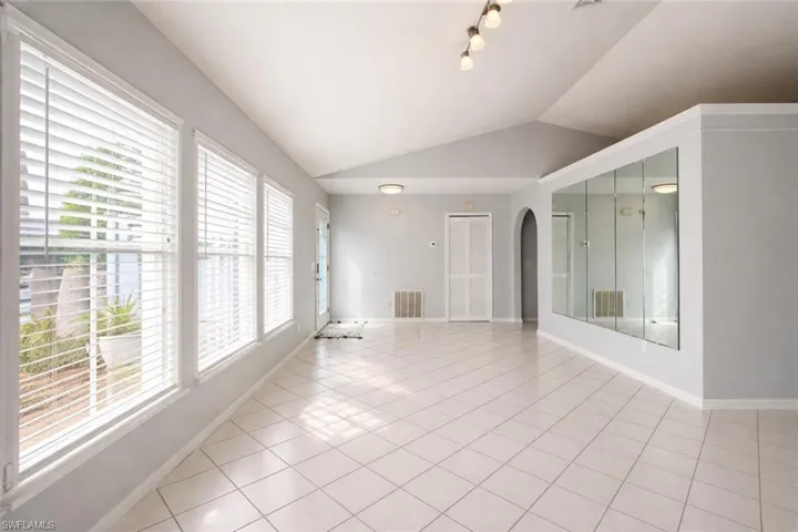 Unfurnished room featuring lofted ceiling, arched walkways, and light tile patterned flooring