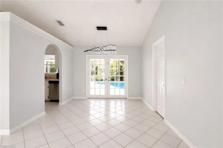 Unfurnished dining area with french doors, plenty of natural light, arched walkways, light tile patterned floors, and vaulted ceiling
