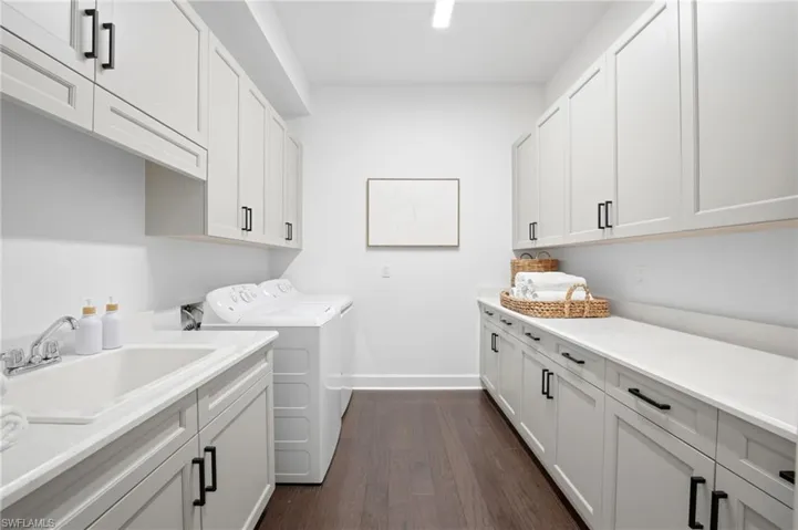 Laundry room featuring shaker-style cabinetry, white solid-surface countertops, wood-finish flooring, and a built-in basin with chrome fixtures