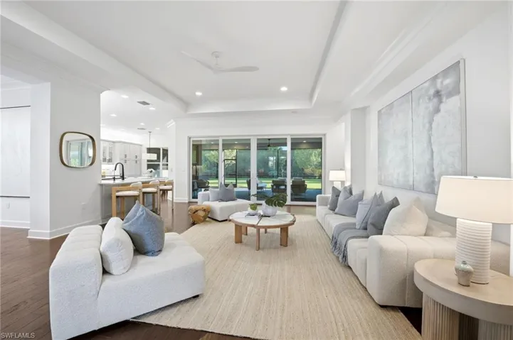 Open-concept interior featuring wood-finish flooring, tray ceilings with recessed lighting, and multi-panel sliding glass doors