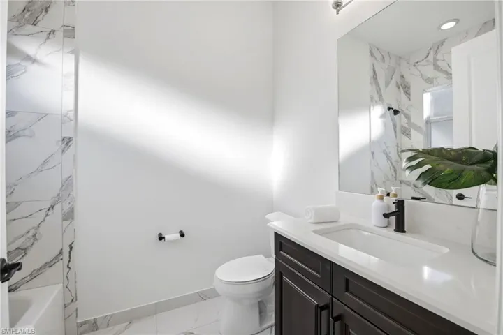 Bathroom featuring a dark wood-finish vanity, light-toned countertop with an integrated sink, matte black faucet, and stone-finish wall tile surrounding the shower area
