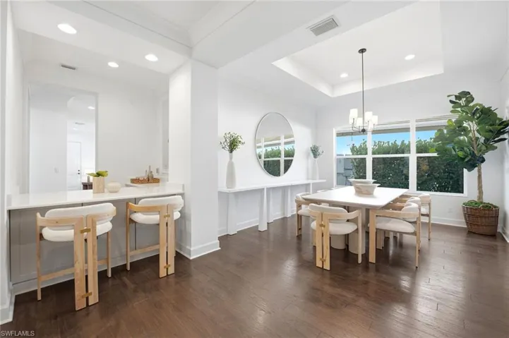 Dining area featuring a recessed tray ceiling, wood-finish flooring, built-in bar with quartz countertop, and oversized windows