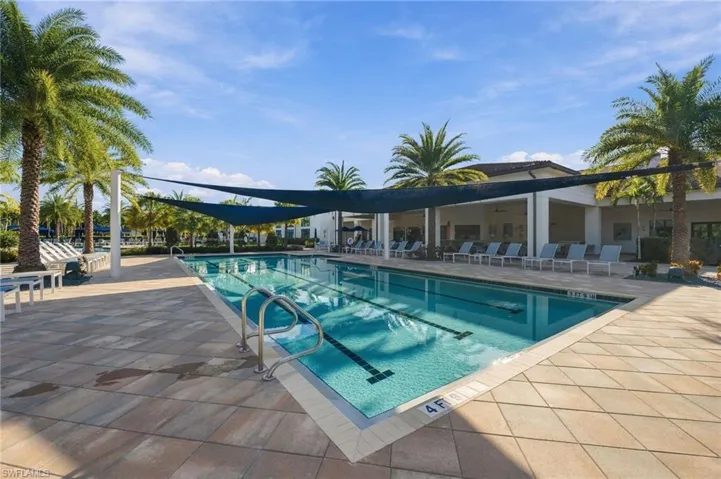 Swimming pool featuring lap lanes, overhead shade sails, tile decking, and surrounding palm trees