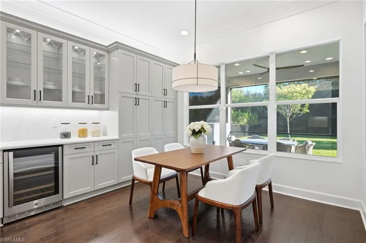 Custom cabinetry with glass-front uppers, built-in under-counter beverage refrigerator, solid surface countertops, wood-finish flooring, and expansive windows