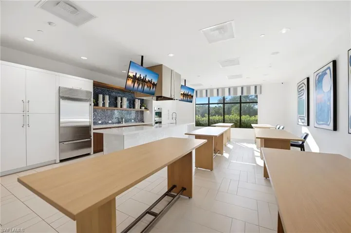 Kitchen area featuring a built-in stainless steel refrigerator, patterned tile backsplash, wood-finish shelving, an expansive island with stone-surface countertop, and large-format tile flooring